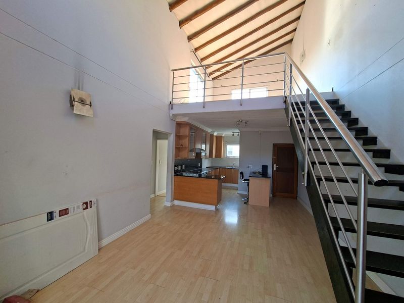 Spacious open-plan living area featuring a mezzanine level, exposed timber rafters, a modern staircase, and a functional kitchen with granite countertops.