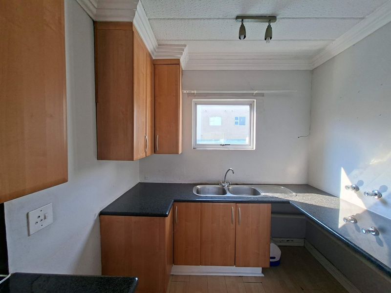 An empty kitchen featuring laminate cabinetry, dark countertops, a stainless steel double sink, and tiled flooring, offering a blank canvas for renovation.