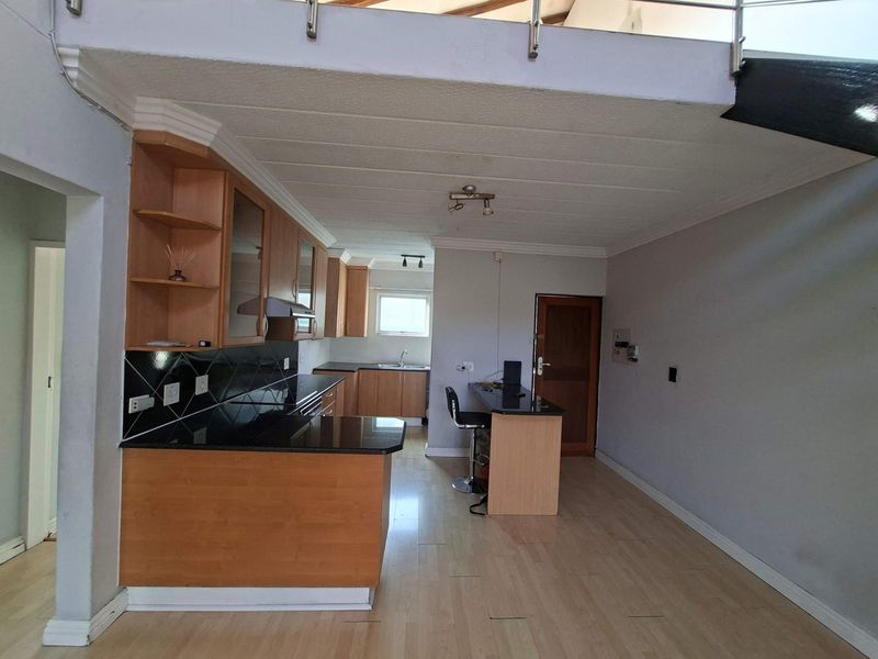 Open-plan kitchen and living area featuring wooden cabinetry, granite countertops, a breakfast bar, and a staircase leading to an upper level.