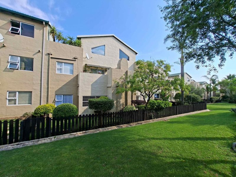 Rear view of the apartment complex featuring a well-maintained lawn, timber fencing, and private balconies with aluminium window frames.
