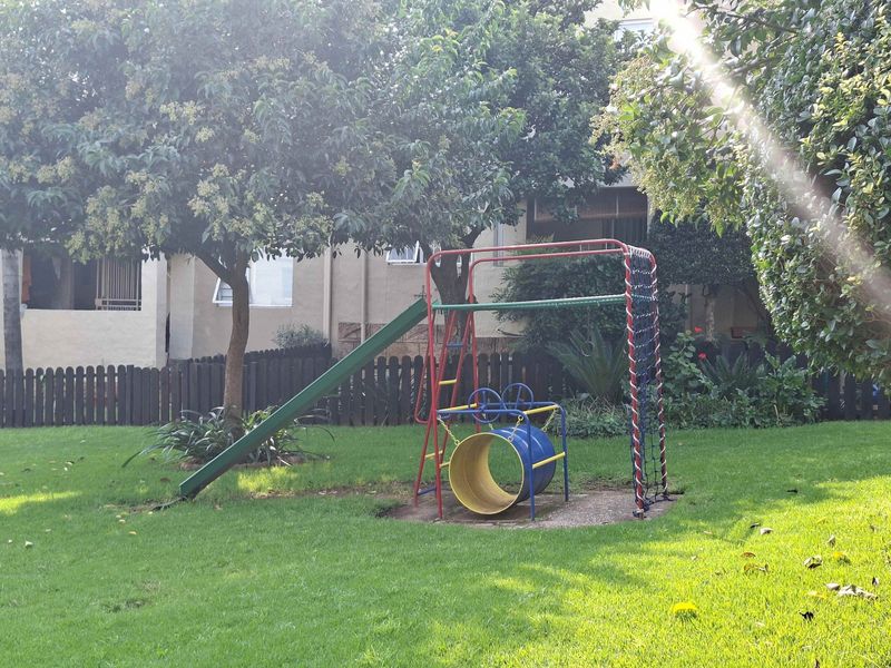 A well-maintained communal garden area featuring a lawn, mature trees, and a timber boundary fence.