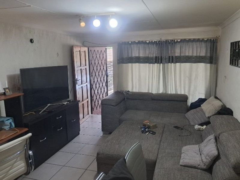 A living room area featuring tiled flooring, track lighting, and a security gate leading to the exterior.