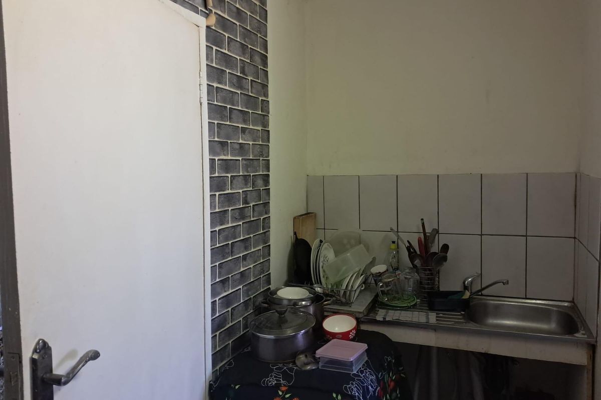 A compact kitchen area featuring a stainless steel sink, tiled backsplash, and decorative brick-effect wall cladding.