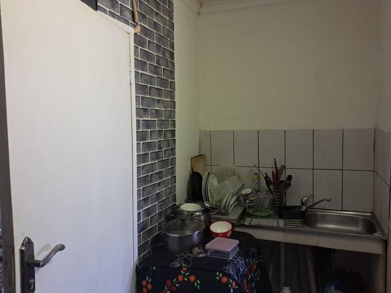 A compact kitchen area featuring a stainless steel sink, tiled backsplash, and decorative brick-effect wall cladding.