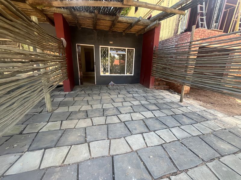 Outdoor patio area featuring stone paving, a timber pergola structure, and rustic wattle fencing, providing a private entrance space.