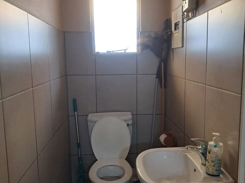 A compact bathroom featuring a pedestal basin and toilet with full-height wall tiling and a small window for natural light.