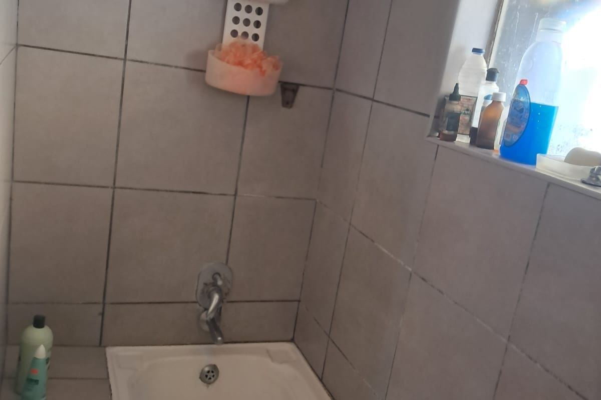 A functional bathroom featuring a standard bathtub with a shower mixer and tiled wall surrounds, requiring some maintenance and cosmetic updates.