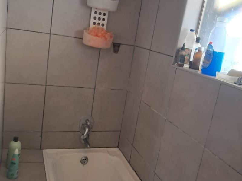 A functional bathroom featuring a standard bathtub with a shower mixer and tiled wall surrounds, requiring some maintenance and cosmetic updates.