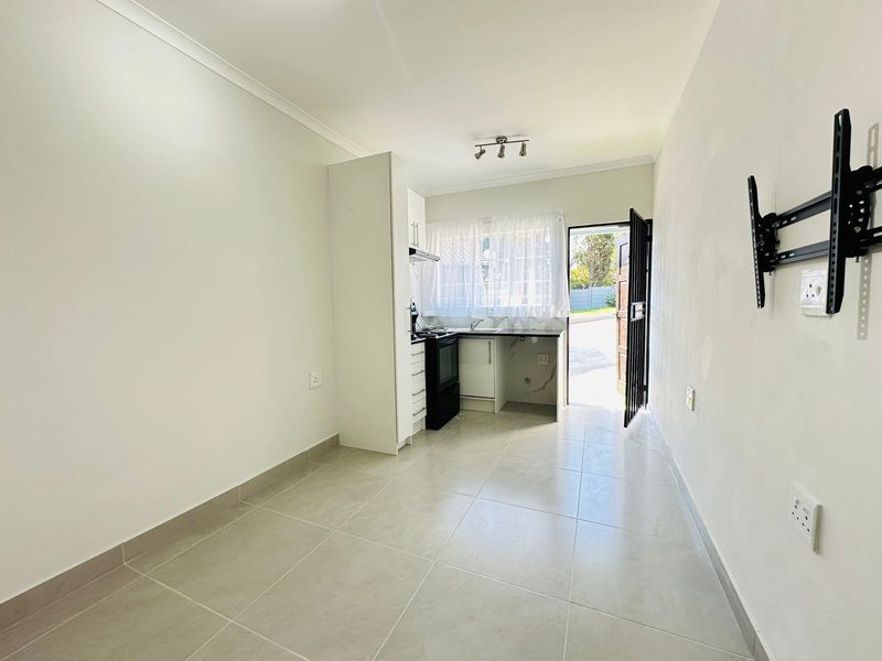 Open-plan living area featuring a compact kitchen with built-in cabinetry, stove, and tiled flooring, leading directly to an exterior entrance.