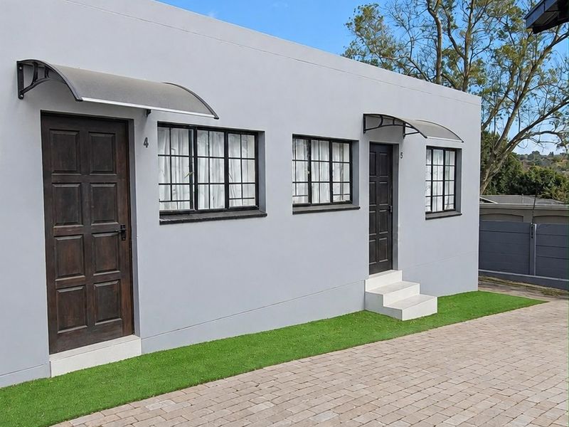 Exterior view of a modern residential building featuring a paved driveway, synthetic lawn, and two separate entrances with protective awnings.