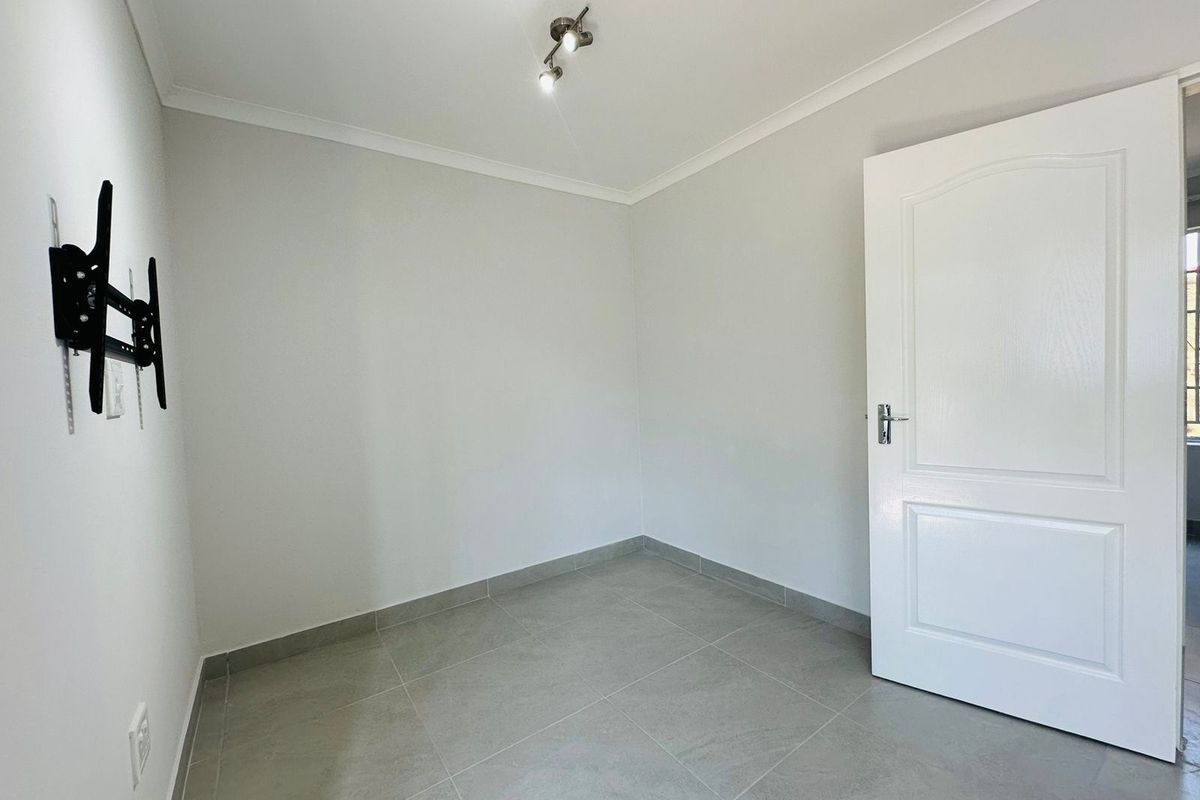 A clean, empty bedroom featuring neutral tiled flooring, coved ceilings, and a modern spotlight fixture, ready for personalization.