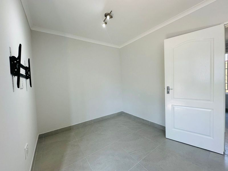 A clean, empty bedroom featuring neutral tiled flooring, coved ceilings, and a modern spotlight fixture, ready for personalization.