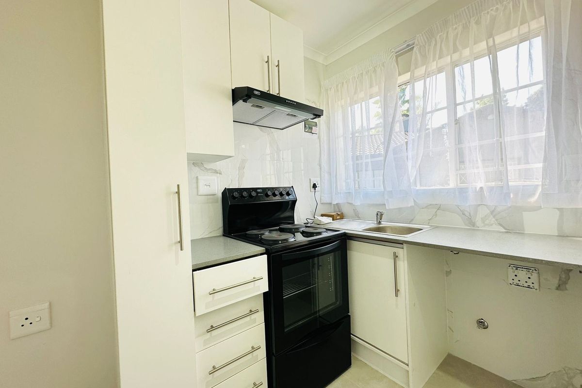A clean, modern kitchen featuring white cabinetry, a black electric stove with extractor fan, and a stainless steel sink with marble-look backsplash.