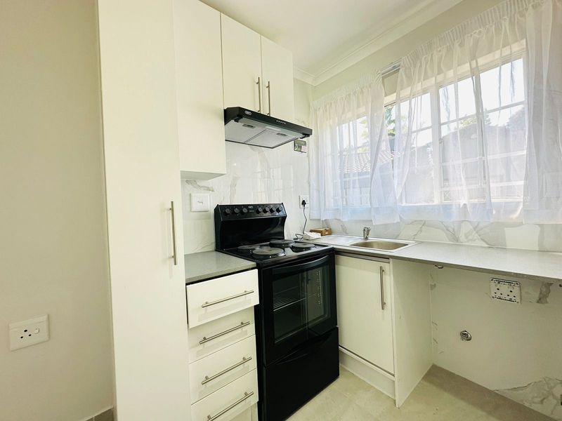 A clean, modern kitchen featuring white cabinetry, a black electric stove with extractor fan, and a stainless steel sink with marble-look backsplash.