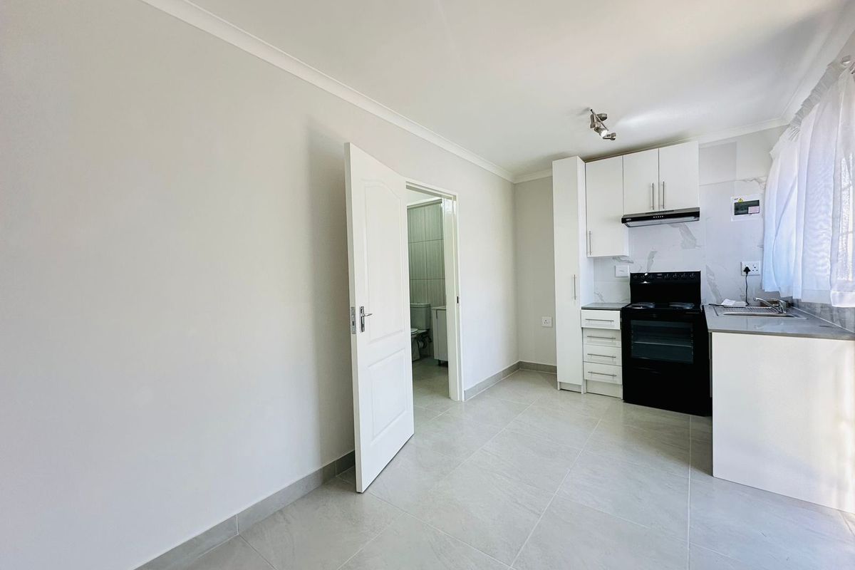 An open-plan kitchen area featuring modern white cabinetry, a black electric stove, tiled flooring, and direct access to an adjacent bathroom.