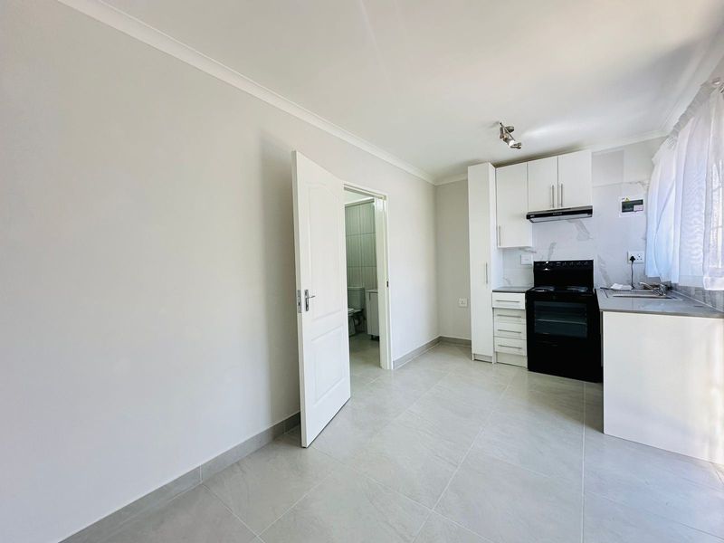 An open-plan kitchen area featuring modern white cabinetry, a black electric stove, tiled flooring, and direct access to an adjacent bathroom.