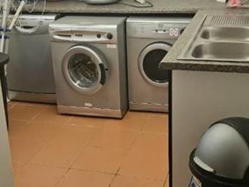 Functional laundry area featuring a double bowl stainless steel sink, laminate countertops, and tiled flooring with space for under-counter appliances.