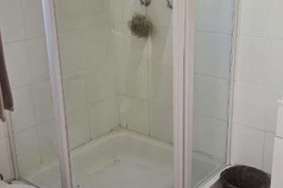 A functional bathroom shower enclosure featuring white wall tiles and a standard shower unit, requiring minor cosmetic updates to refresh the space.