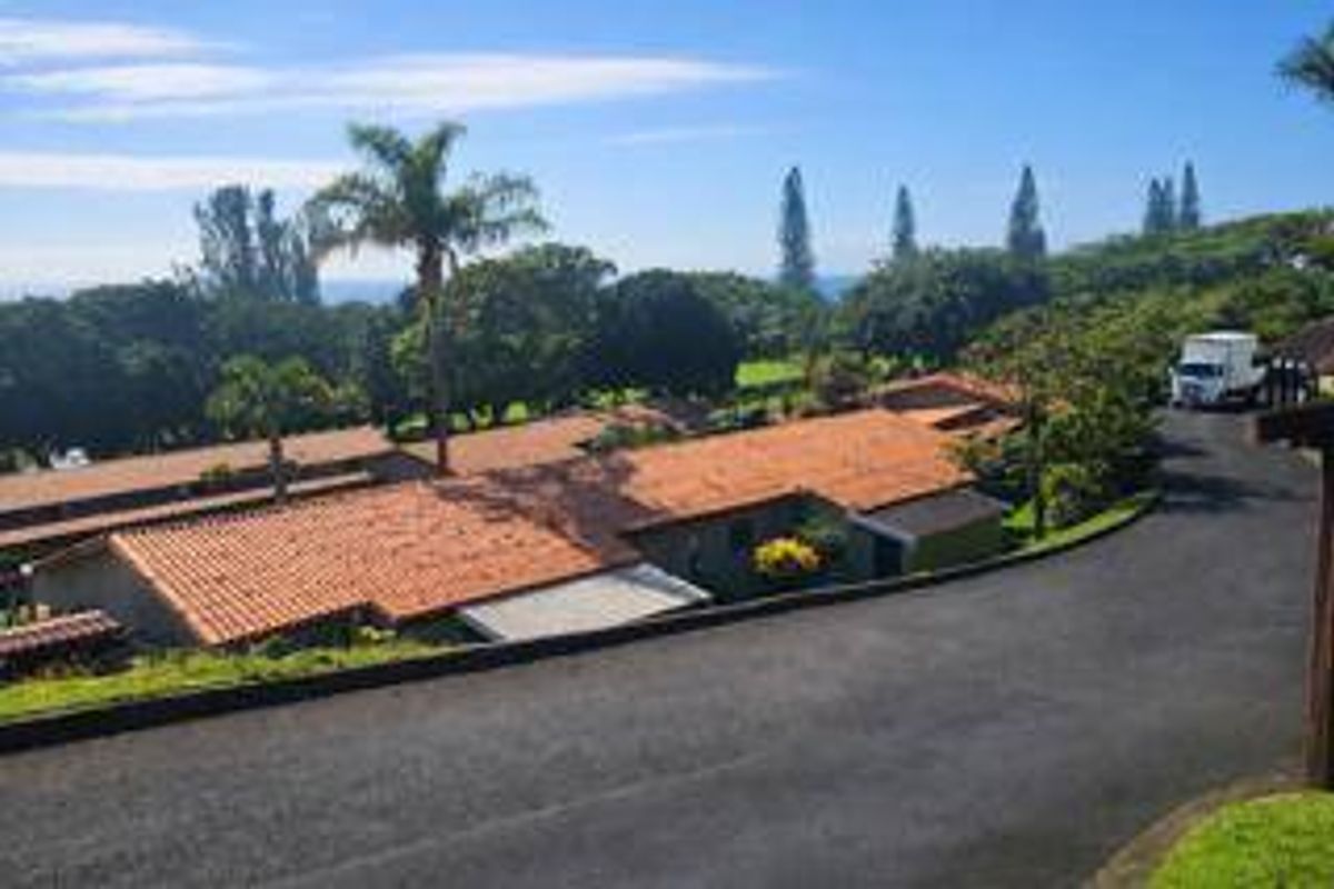 An elevated aerial view of the townhouse complex featuring tiled roofs, surrounding lush greenery, and a paved driveway.