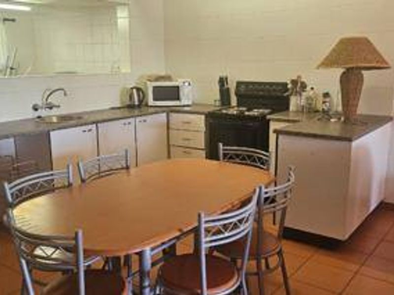 Open-plan kitchen and dining area featuring dated cabinetry, laminate countertops, a freestanding stove, and tiled flooring throughout.