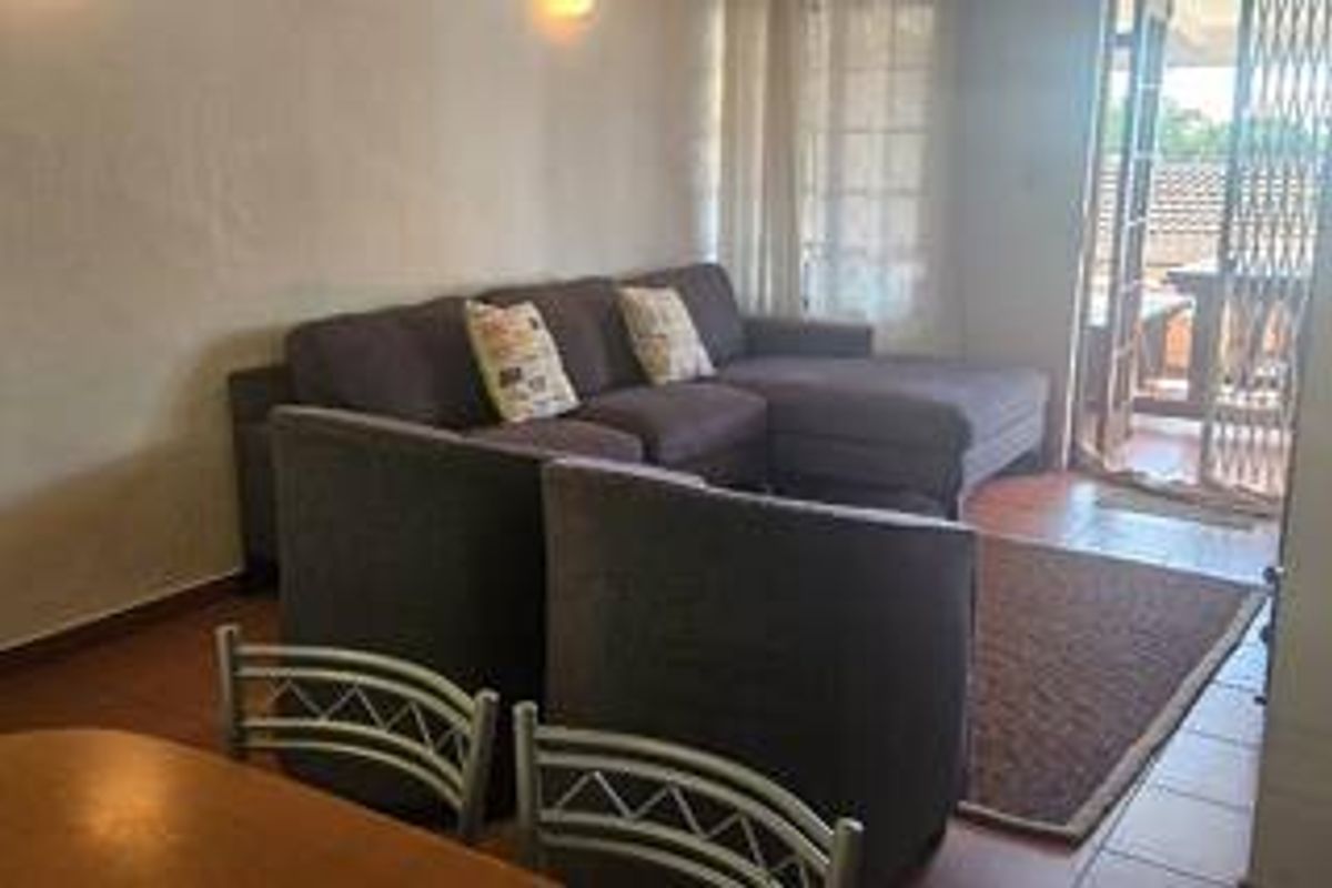 A living room area featuring tiled flooring and a sliding glass door with a security gate leading to an outdoor patio space.