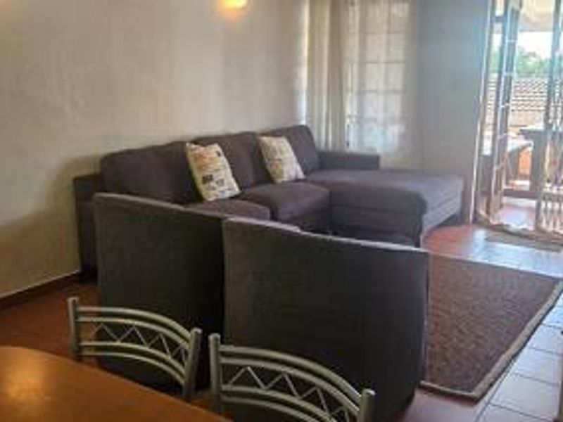 A living room area featuring tiled flooring and a sliding glass door with a security gate leading to an outdoor patio space.