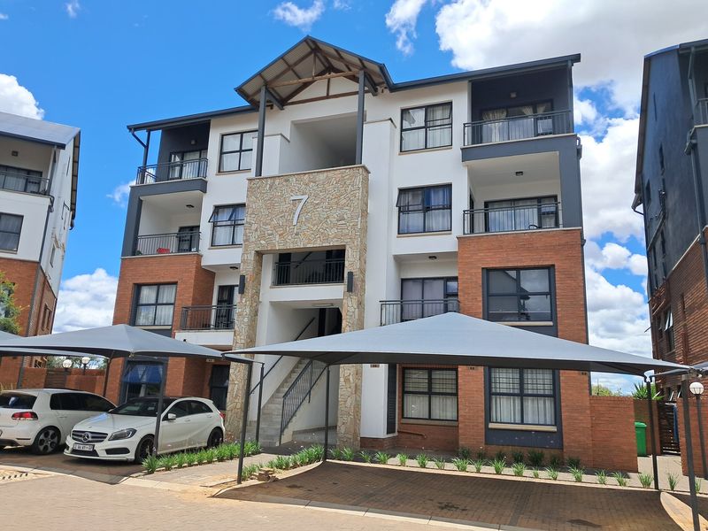 Front elevation of a modern multi-story apartment building featuring stone and brick facade, private balconies, and dedicated shade cloth parking bays.