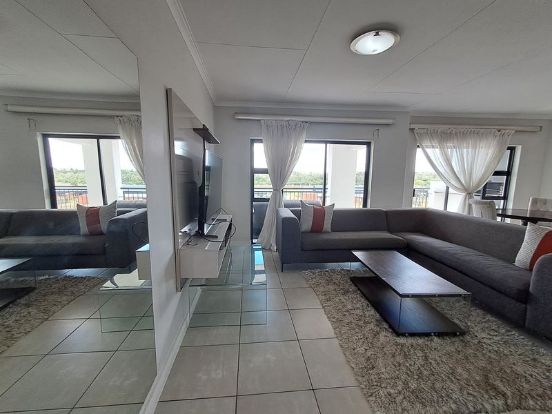 Spacious living room featuring large sliding glass doors, neutral tiled flooring, and a prominent wall-mounted mirror, offering a bright and open atmosphere.