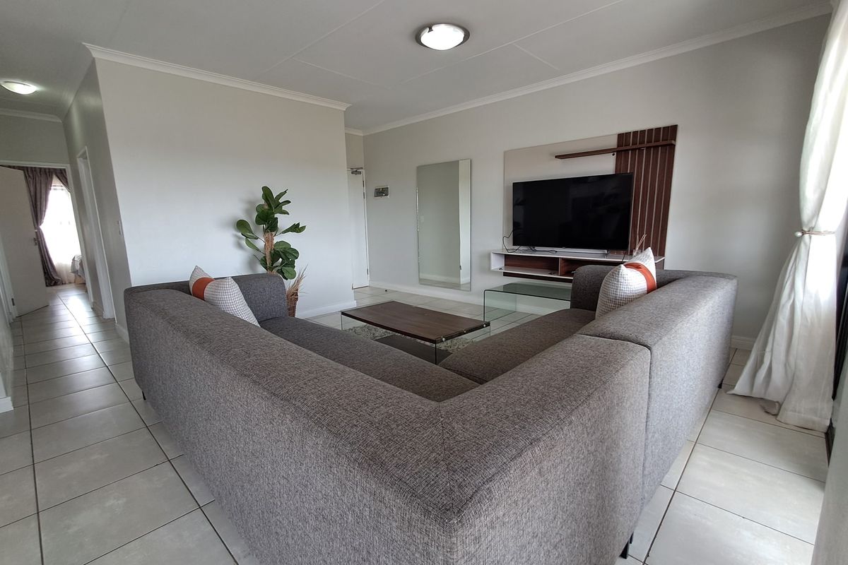 A well-maintained living room featuring neutral tiled flooring, cove cornicing, and a built-in media console unit.
