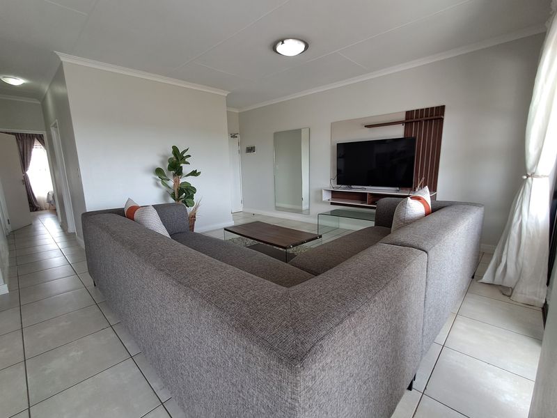 A well-maintained living room featuring neutral tiled flooring, cove cornicing, and a built-in media console unit.
