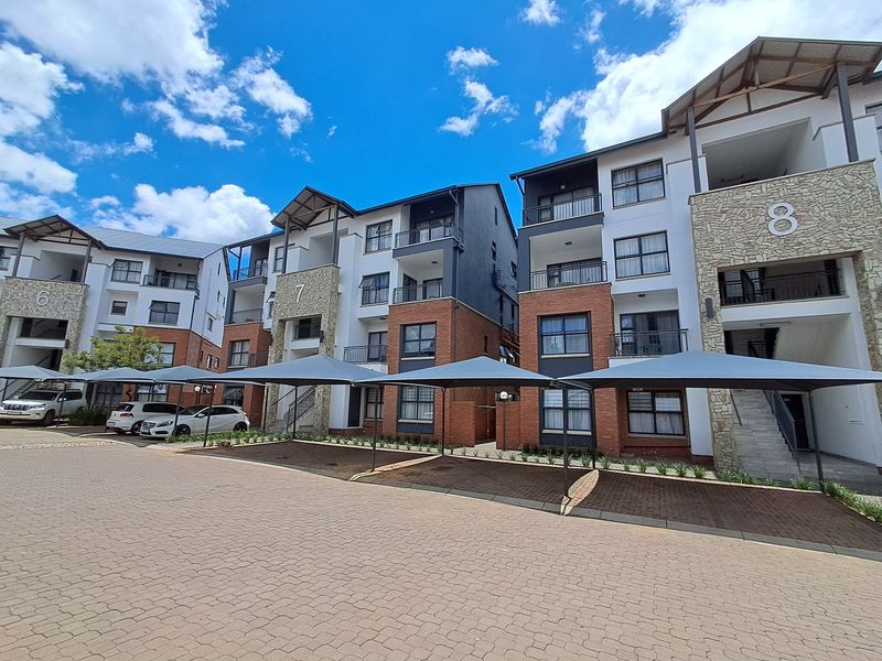 Exterior view of a modern apartment complex featuring brick and stone facade, private balconies, and covered parking bays.