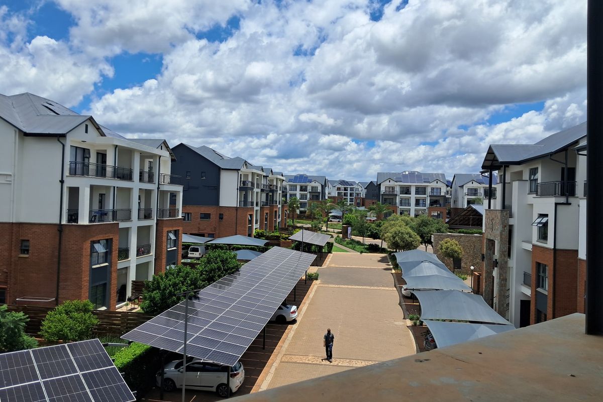 An elevated view of a modern apartment complex featuring paved driveways, solar panel carports, and well-maintained multi-story residential buildings.