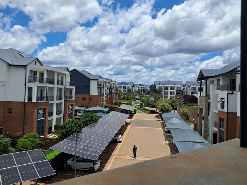 An elevated view of a modern apartment complex featuring paved driveways, solar panel carports, and well-maintained multi-story residential buildings.