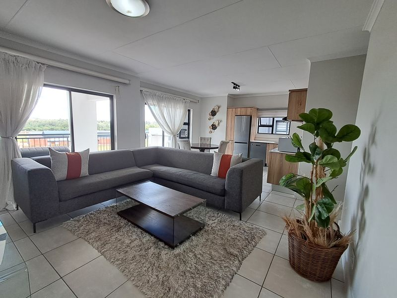 Spacious open-plan living and kitchen area featuring tiled floors, modern cabinetry, and large sliding doors leading to an outdoor balcony.