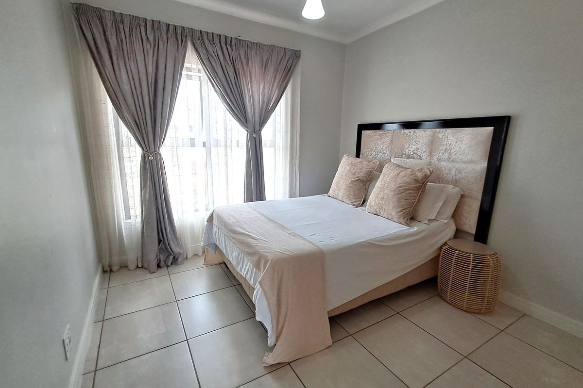A well-maintained bedroom featuring neutral tiled flooring and large windows with installed curtain tracks, providing a bright and comfortable living space.