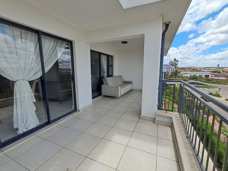 A spacious covered balcony featuring tiled flooring, a metal balustrade, and large sliding glass doors providing access to the interior living space.