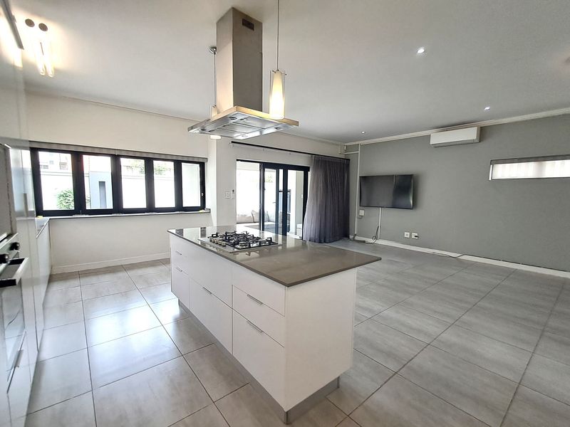 Spacious open-plan living and kitchen area featuring a central island with gas cooktop, modern cabinetry, tiled floors, and direct access to the patio.
