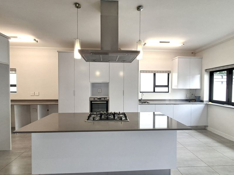 Modern kitchen featuring a central island with a gas hob, built-in oven, extractor fan, stone countertops, and ample white cabinetry.