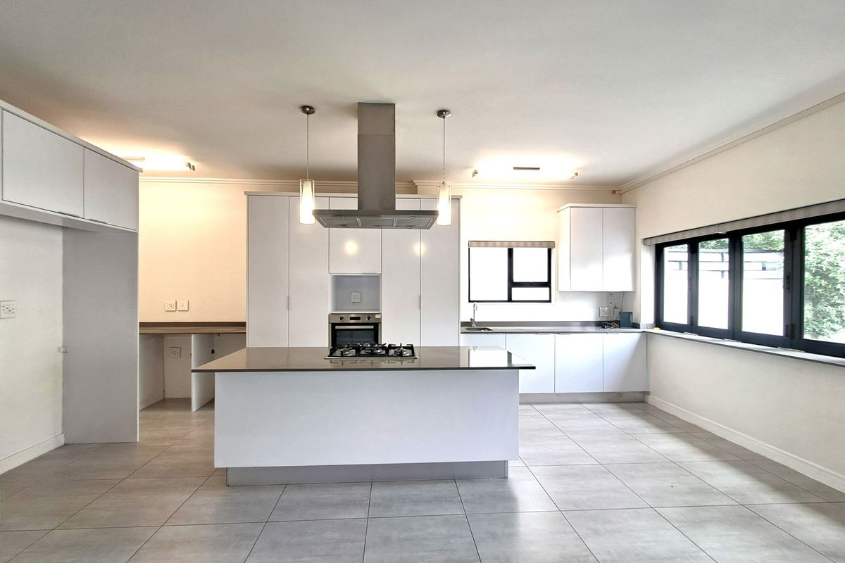 Modern, spacious kitchen featuring a central island with gas hob, built-in oven, sleek white cabinetry, and large windows providing ample natural light.