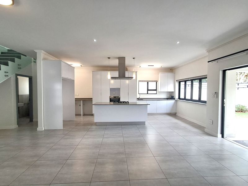 Spacious open-plan kitchen and living area featuring modern white cabinetry, a central island with gas hob, tiled floors, and seamless access to the outdoor space.