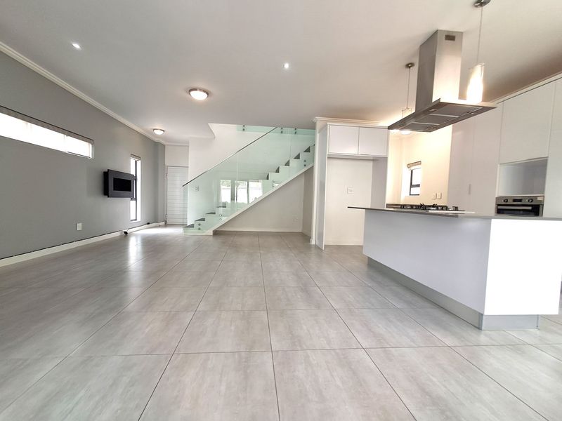 Spacious open-plan living and kitchen area featuring modern porcelain tiling, a sleek glass-railed staircase, and a contemporary kitchen with integrated appliances.