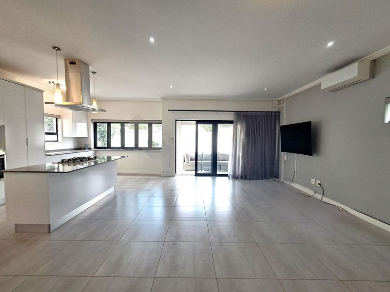 Spacious open-plan living and kitchen area featuring modern tiled flooring, a central kitchen island with gas hob, and seamless access to the outdoor patio.