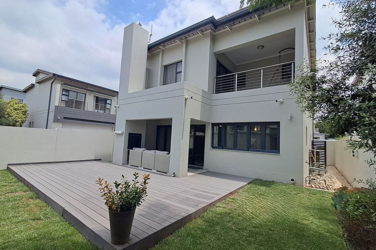 Rear view of a modern townhouse featuring a composite deck, covered patio with built-in fireplace, and an upper-level balcony with stainless steel railings.