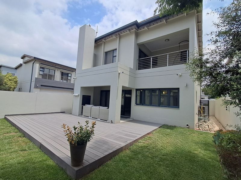 Rear view of a modern townhouse featuring a composite deck, covered patio with built-in fireplace, and an upper-level balcony with stainless steel railings.