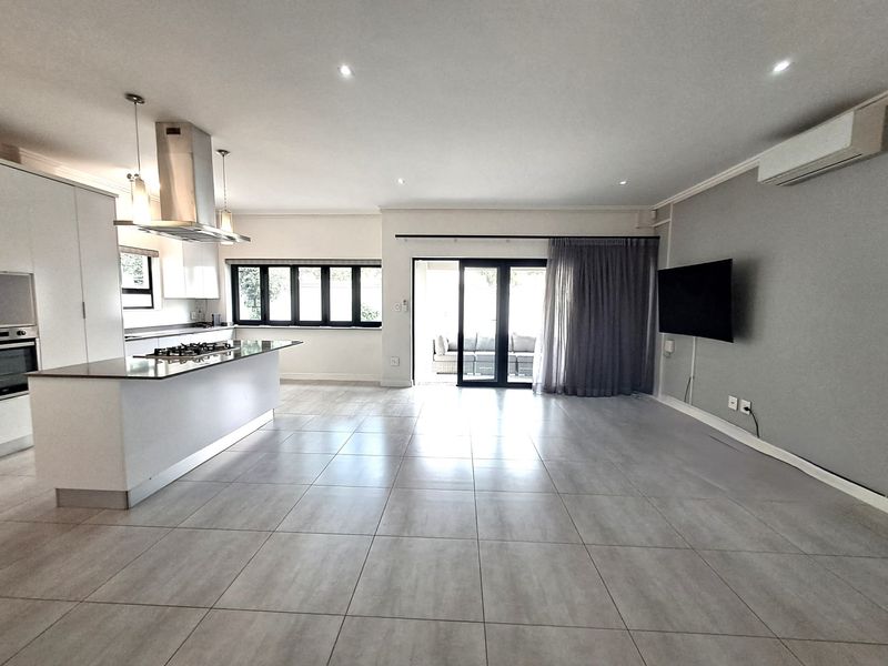 Spacious open-plan living and kitchen area featuring modern tiled floors, a central island with gas hob, and seamless access to the outdoor patio.