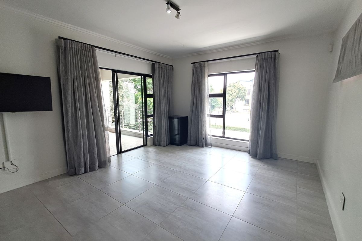 A bright and spacious living area featuring neutral tiled flooring, large windows, and a sliding glass door leading to an outdoor patio space.