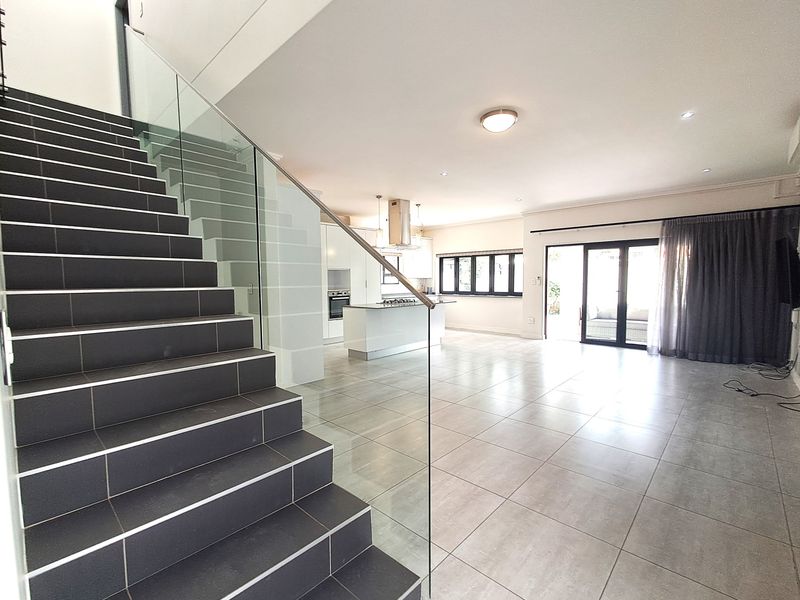 Spacious open-plan living area featuring a modern kitchen with island, tiled staircase with glass balustrade, and large sliding doors leading to the outdoors.