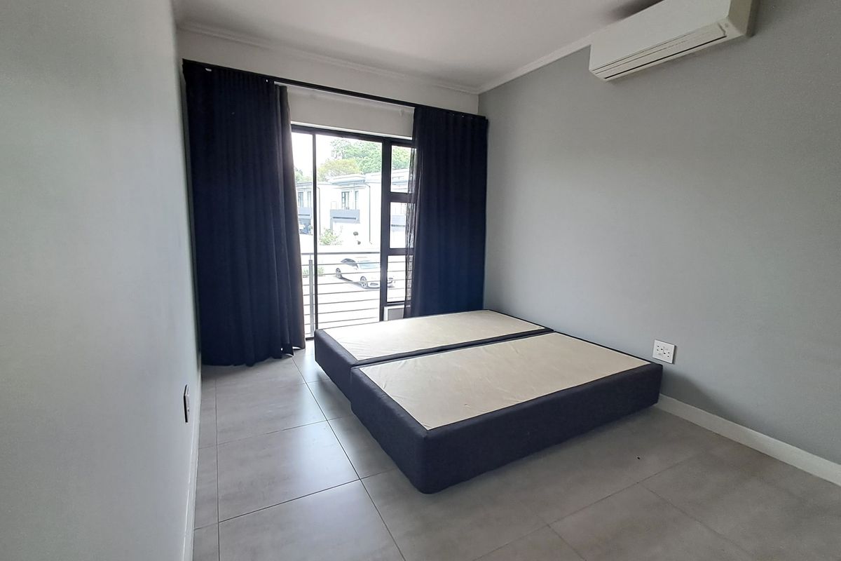 A bright bedroom featuring neutral tiled flooring, a wall-mounted air conditioning unit, and a sliding glass door leading to a balcony.