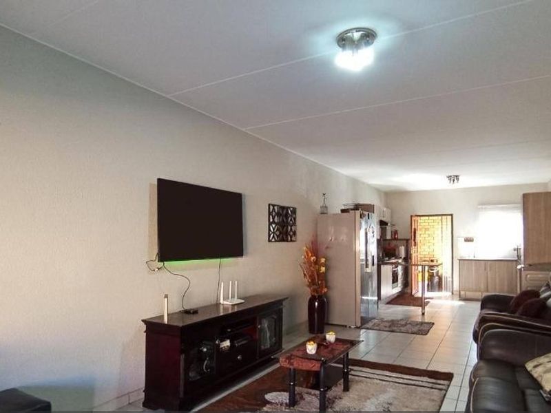 Open-plan living area featuring tiled flooring and a connected kitchen space with built-in cabinetry and appliances.