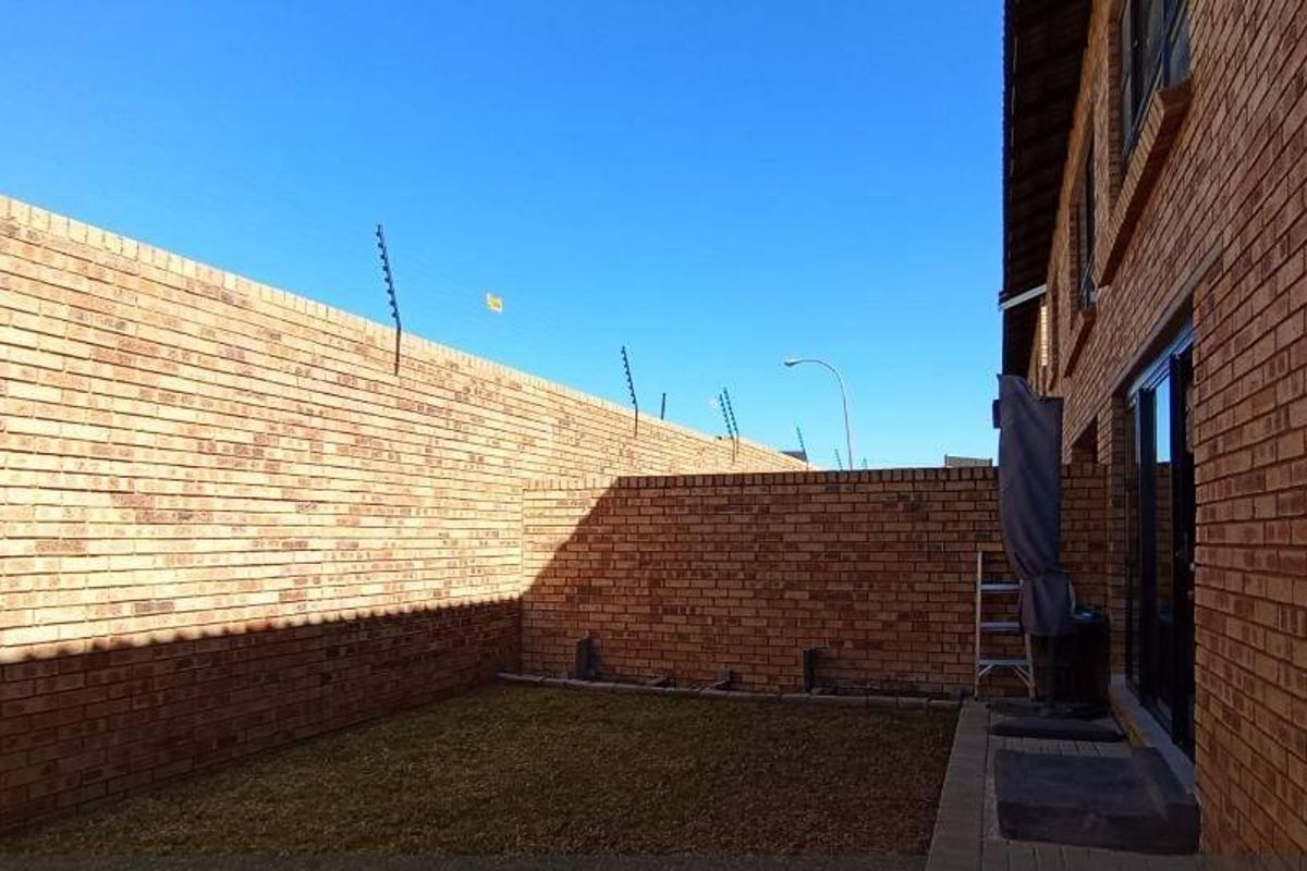 A private rear courtyard featuring a face brick boundary wall with electric fencing, a paved walkway, and direct access to the apartment via sliding doors.